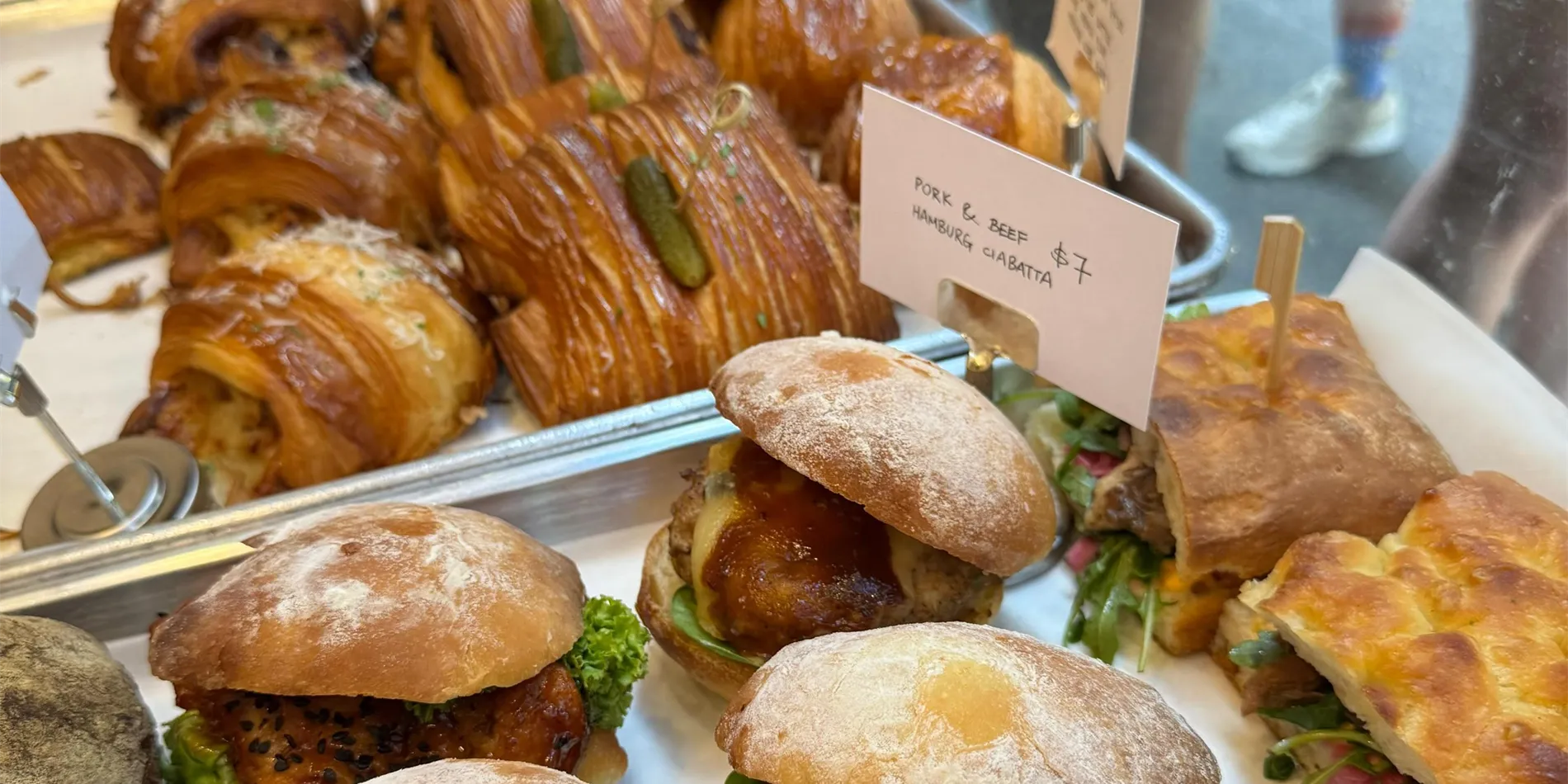 The Wild Honey Pie counter — croissants, ciabatta sandos and focaccia on stainless trays with hand-written price cards
