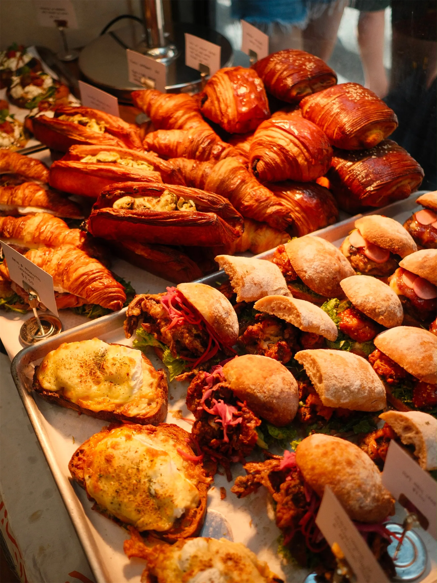 The counter at Wild Honey Pie — croissants, pain suisse, ciabatta sandos and croque madame under warm morning light