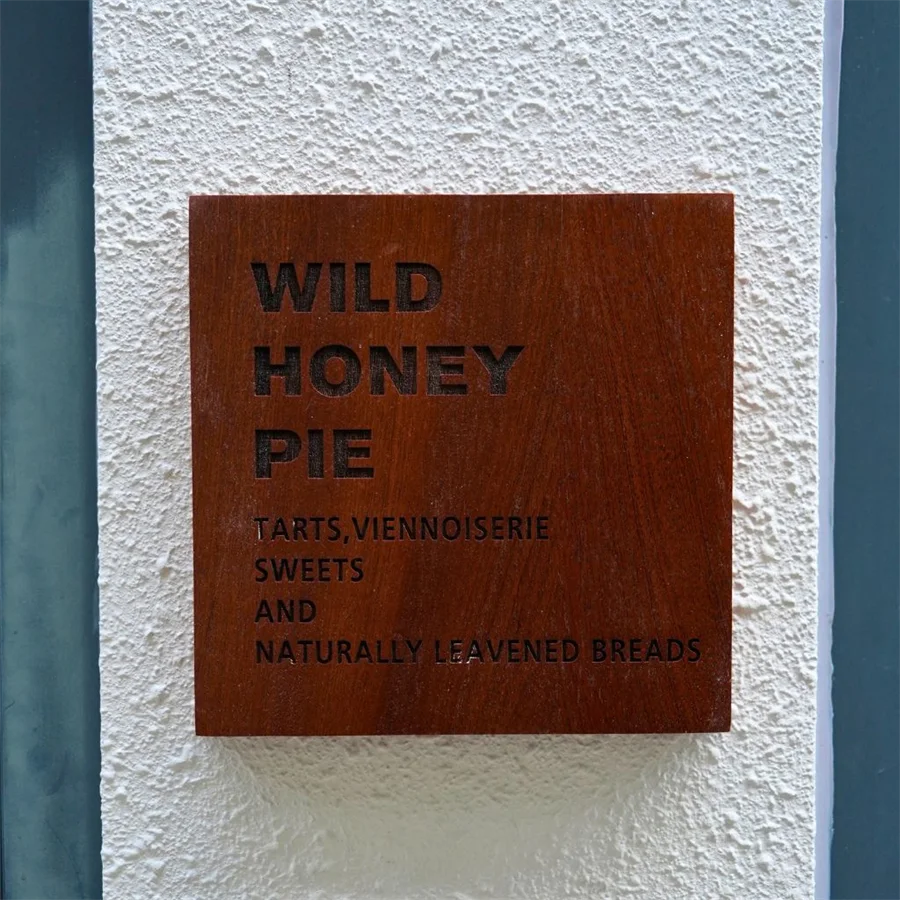 The engraved wooden plaque at Wild Honey Pie reading wild honey pie, tarts, viennoiserie, sweets and naturally leavened breads