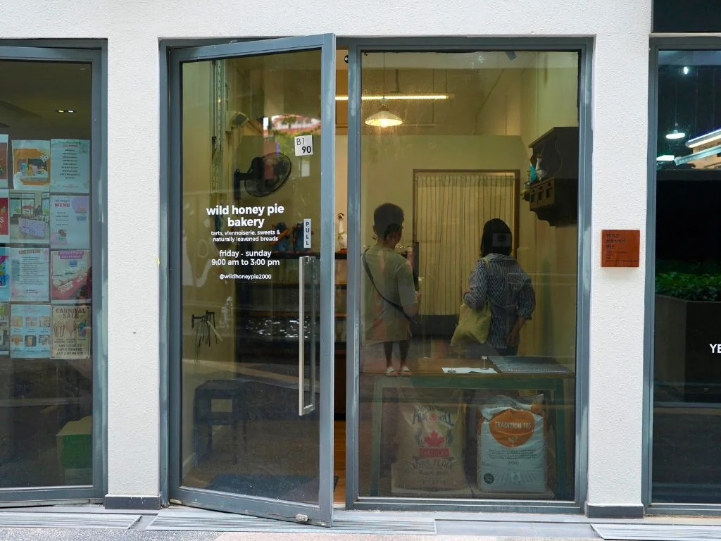 The glass door at B1-90 with wild honey pie bakery in white vinyl and the unit placard